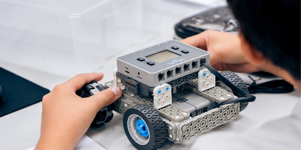 Un chico ajusta las ruedas del robot VEX que está armando sobre la mesa