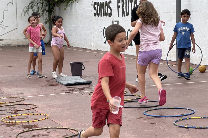 Chicos corriendo entre aros en el patio, con vasos de agua en la mano