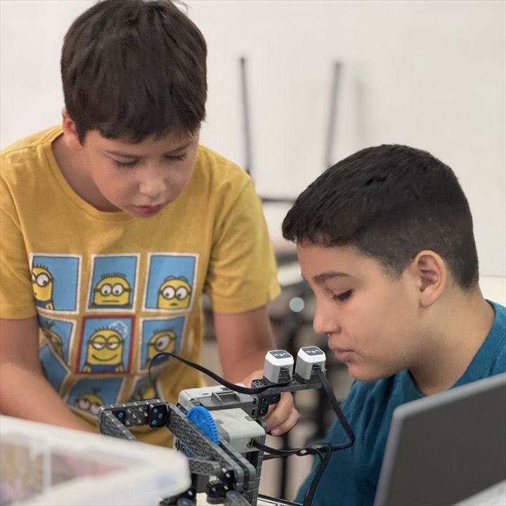 Dos chicos arman un robot con piezas de robótica al lado de una notebook