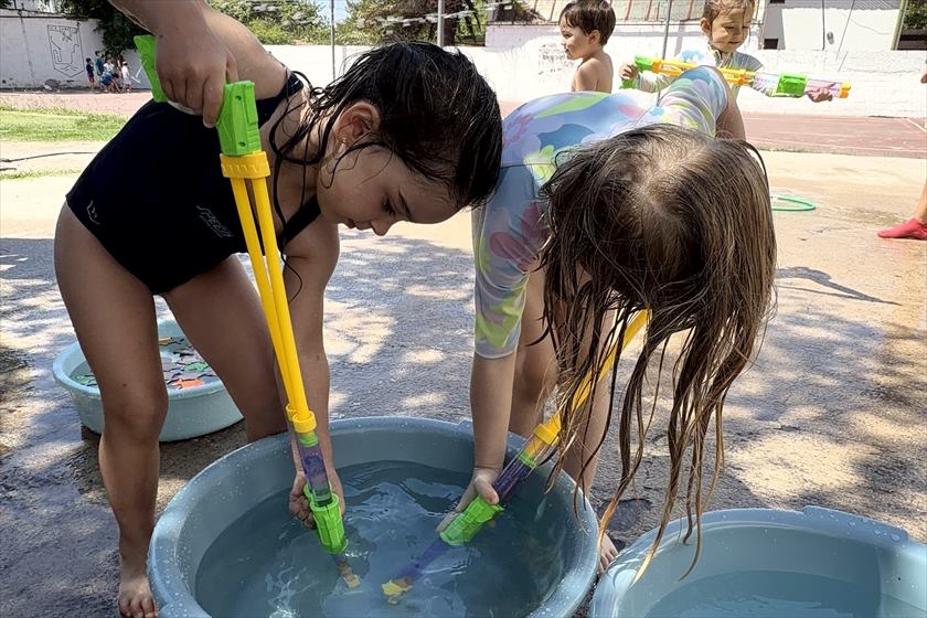 Chicos cargando pistolas de agua en palanganas, al sol