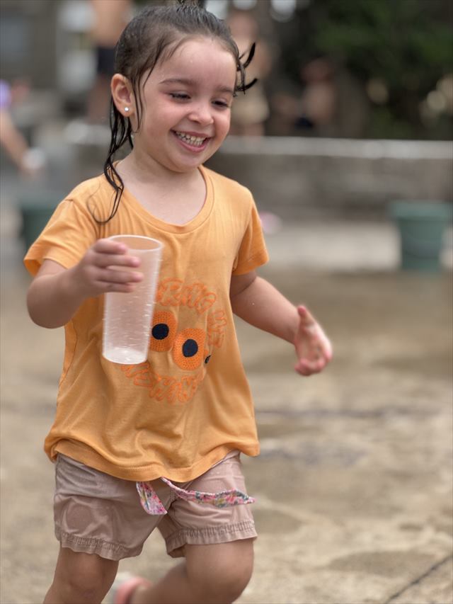 Una nena corre al sol con un vaso en la mano