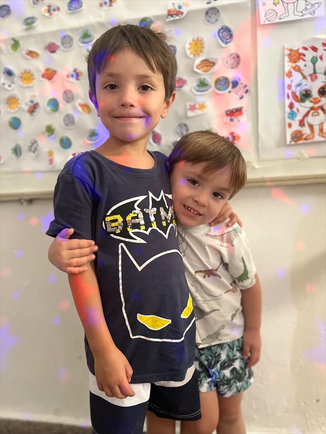 Dos chicos abrazados delante de la pared con los trabajos del taller